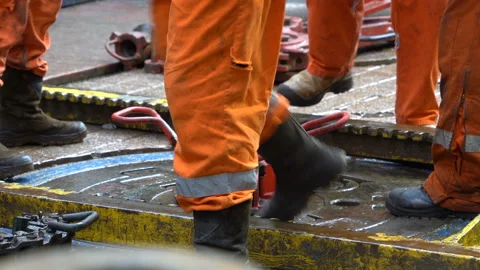 Drilling platform. Rotor table. Manual slips installed. Legs in orange coveralls Stock Footage 196259099