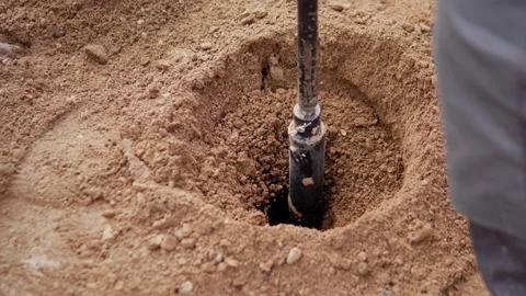 Drilling tool set deeper inside circular sandy soil pit, disturbing loose earth Stock Footage 344877083