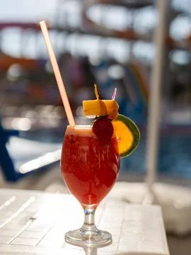 A drink sits on a table by the pool, decorated with slices of fruit. A stra.. Foto stock