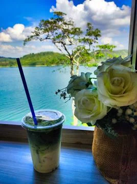 A drink sits on a table with a view of water and trees in the background du.. Stock Photos