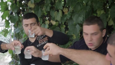 Drink vodka from glasses. two men. at the table in jackets. outdoors Video stock 113792636