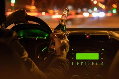 Drinking beer while driving car. Man hold bottle alcohol in hand at the night Stock-Fotos