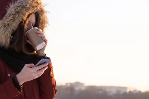 Drinking coffee and using smartphone outdoors in winter Stock Photos