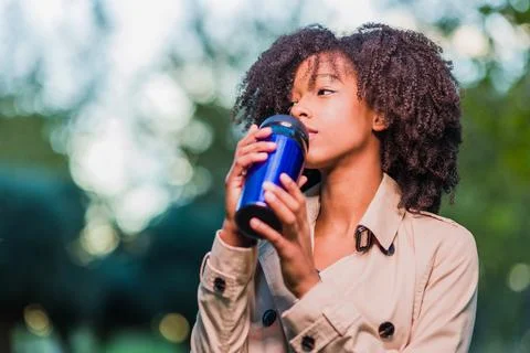 Drinking coffee drink outdoors in winter from a thermos. Latinx woman with afro Stock Photos