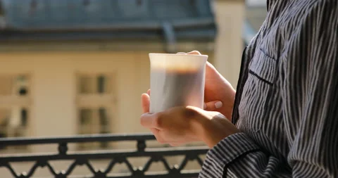 Drinking coffee or tea. girl looks out over the rooftops of the city morning Stock Footage 151784307