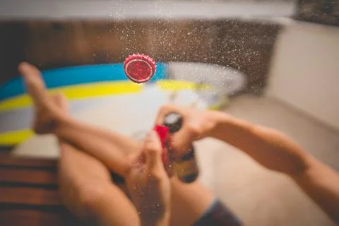 Drinking cold beer. Opening bottle of beer. Focus on the cap in the air. Stock Photos