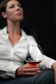 Drinking glass filled with alcohol held by sad looking woman in business clothes Stock Photos