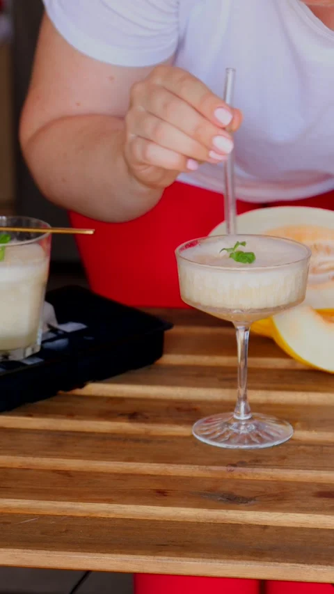 Drinking melon cocktail with white wine and ice using straw in elegant coupe Stock Footage 313793955