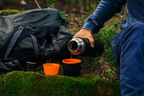 Drinking tea during hike. Man hand pouring hot tea from thermos into 2 cup's Stock Photos