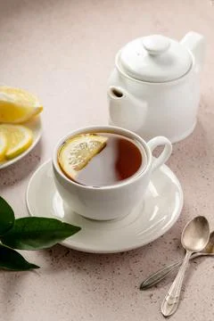 Drinking tea, white ceramic cup and tea pot with black tea and lemon slice. Stock Photos