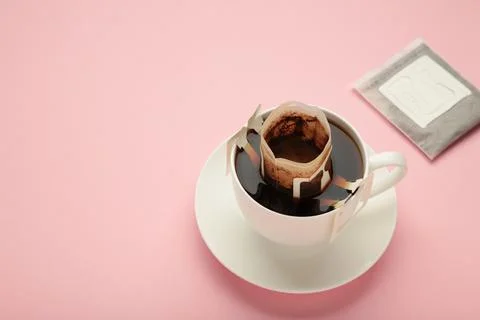 Drip coffee bag with ground coffee in cup on pink background Stock Photos
