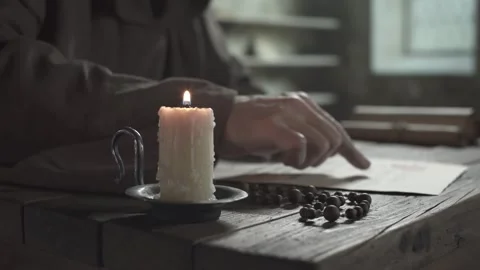 Dripping candle, rosary beads on table, monk guiding finger along text lines Stock Footage 338991010