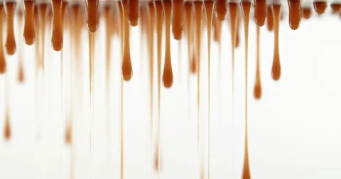 Dripping caramel droplets flowing down liquid sweet sauce on white background Stock Footage 224519824