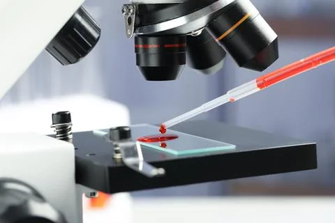 Dripping sample of red liquid onto slide under microscope in laboratory, clos Stock Photos