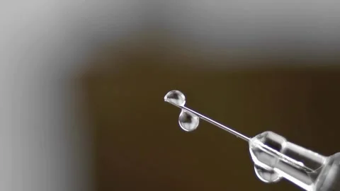 Dripping syringe against blurred gray background. Side view, macro shot Stock-Footage 336587304