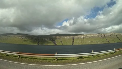 Drive-by view of Sundini strait and green slopes with waterfalls, Faroe Islands Stock Footage 339794140