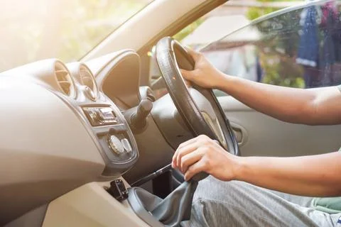 The driver adjusts the gear while gripping the steering wheel inside the car. Stock Photos