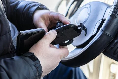 A driver adjusts a smartphone in a suction cup mount on a vehicle dashboard.. Stock Photos