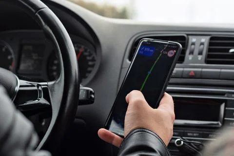 Driver in a black leather jacket checks a navigation app on a smartphone whil Stock-Fotos