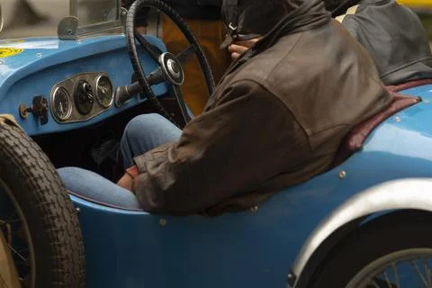Driver in brown leather jacket sitting in vintage blue open sports car cockpit Stock Photos