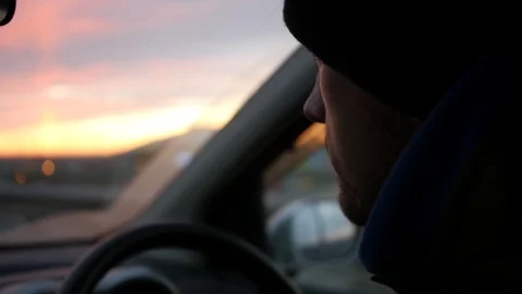 The driver in the cap rides behind the wheel of the car to meet the sunset. HD Stock Footage 82394227