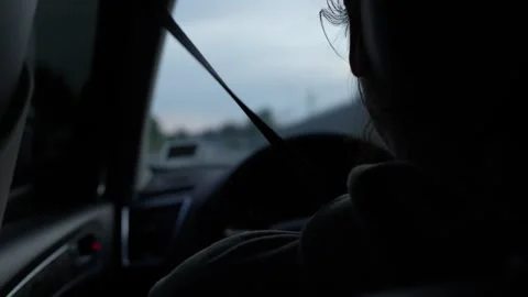 Driver in a car behind the wheel at dusk, over the shoulder view Stock Footage 312288891
