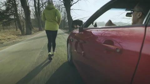 The driver of the car drives alongside the running girl and slaps her butt. Stock Footage 87919518