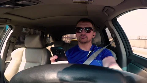 The driver of the car looks and types the text on the smartphone on the move Video stock 74423261