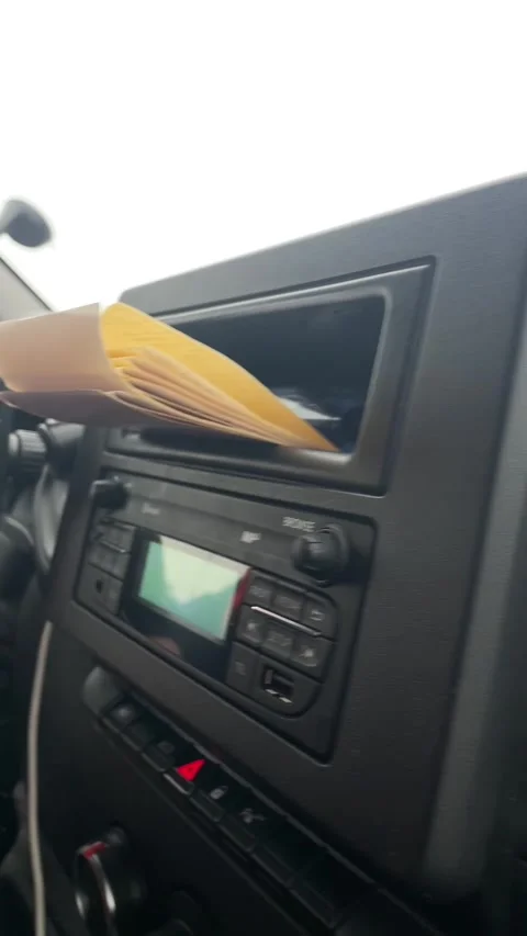 Driver cautiously tucks envelope into dashboard storage space during delivery Видео 335366219