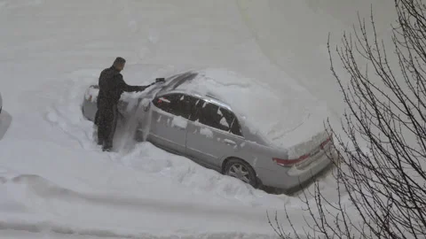 Driver Clears Snow from Car in Snow-Covered Parking Lot Stock Footage 304609182