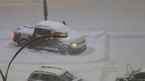 Driver Clears Snow from Car in Snow-Covered Parking Lot Video stock 304618253