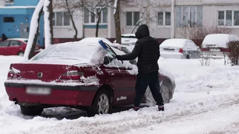 Driver clears snow from a car in the yard in winter, slow motion Stock Footage 291778438