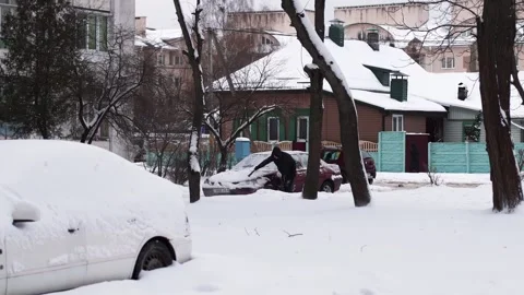 Driver clears snow from a car in the yard in winter, slow motion Stock Footage 313892432