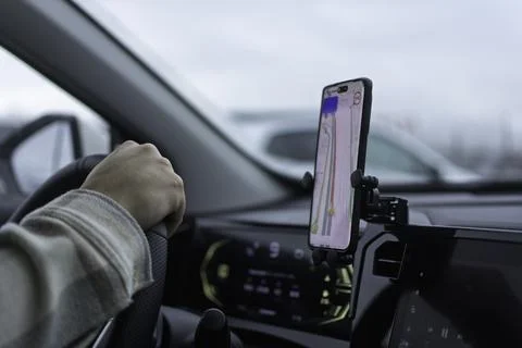 Driver confidently steers car with navigation app displayed on smartphone, Stock Photos