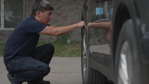 Driver crouching to inspect car tire condition on urban street Stock Footage 342627732