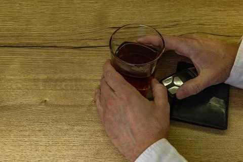 A driver dressed in an elegant shirt picks up a glass of whiskey with ice f.. Stock Photos