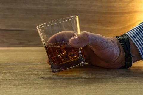 A driver dressed in an elegant shirt picks up a glass of whiskey with ice f.. Stock Photos
