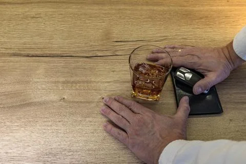 A driver dressed in an elegant shirt picks up a glass of whiskey with ice f.. Stock Photos