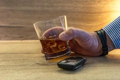 A driver dressed in an elegant shirt picks up a glass of whiskey with ice f.. Stock Photos