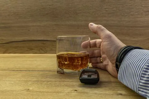 A driver dressed in an elegant shirt picks up a glass of whiskey with ice f.. Stock Photos