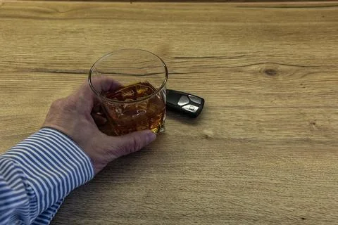 A driver dressed in an elegant shirt picks up a glass of whiskey with ice f.. Stock Photos