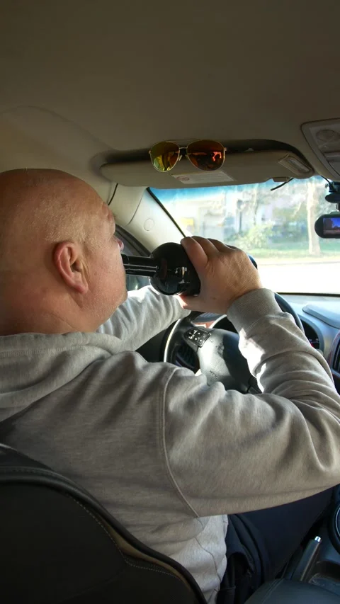 The driver drinks strong alcohol while driving - vertical video Видео 320357428
