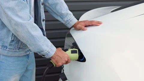 The driver of the electric car inserts the electrical connector to charge the Stock Footage 251767541