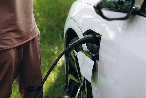 The driver of the electric car inserts the electrical connector to charge the Stock Photos