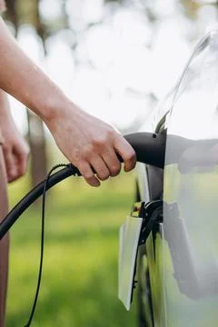 The driver of the electric car inserts the electrical connector to charge the Stock Photos