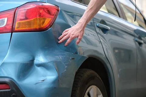 Driver hand examining dented car with damaged fender parked on city street side Stock Photos