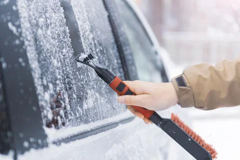 Driver hand with scraper removes ice from the car windscreen after heavy snow Stock Photos