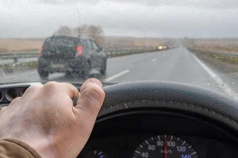 Driver hand on the steering wheel inside the car and raindrops on the windshield Stock Photos