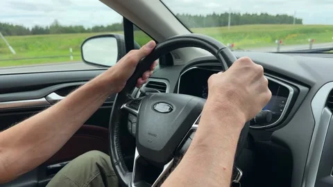 Driver hands holding steering wheel driving car on suburban road on overcas.. Stock Footage 343260437