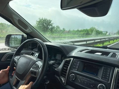 Driver holding steering wheel inside a car while driving on a rainy highway Foto stock
